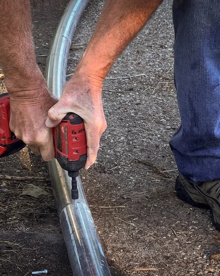 Work boots and hands steadying a drill against a steel pipe.